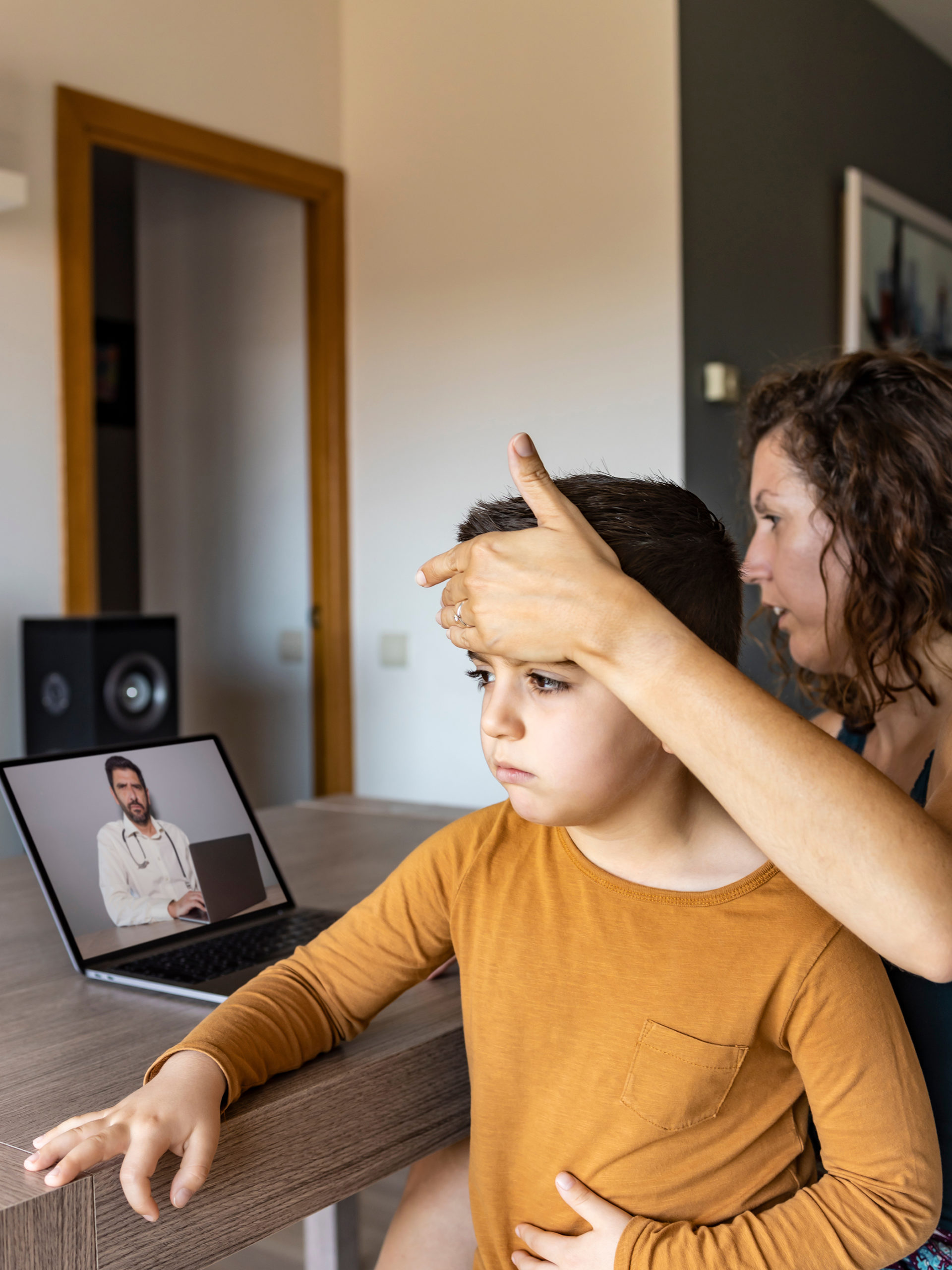 Worried Mother Video Chatting With Doctor On Laptop while touching son's forehead