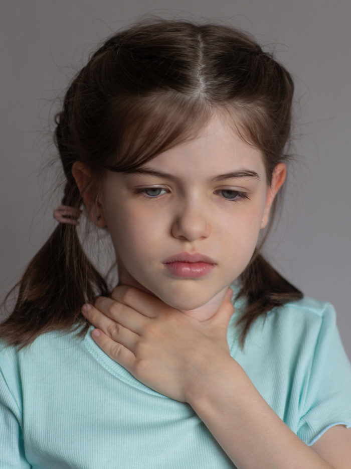 sick little girl holding her throat with a sad expression on her face