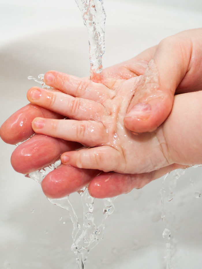 parent washing baby hand with water in the sink