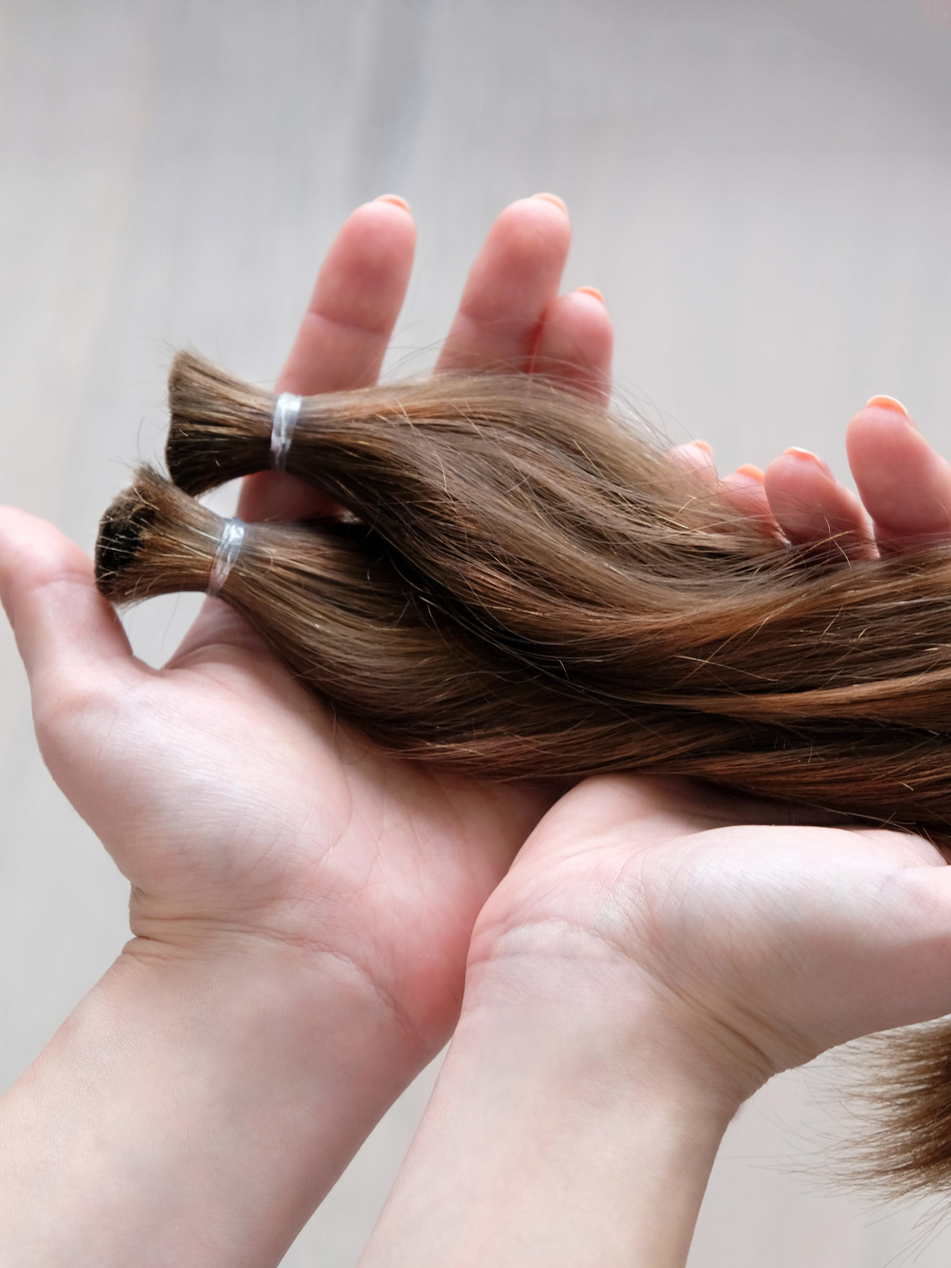woman donating two chopped brown hair long pony-tails