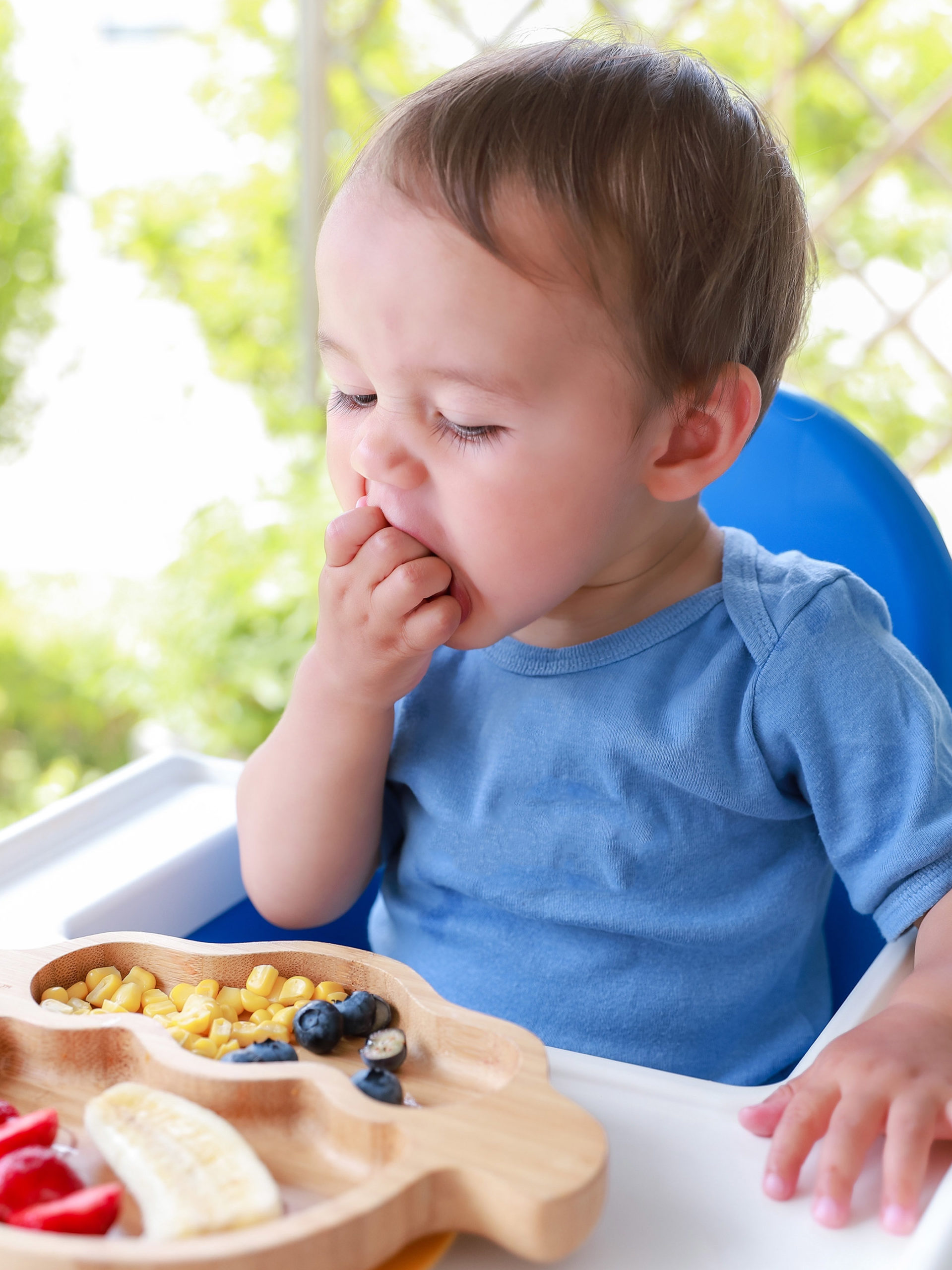 boy eating fruit and veggies by himself on high chair