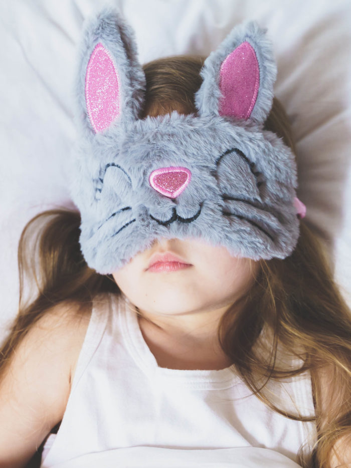 Little girl sleeping while wearing grey bunny plush sleep mask