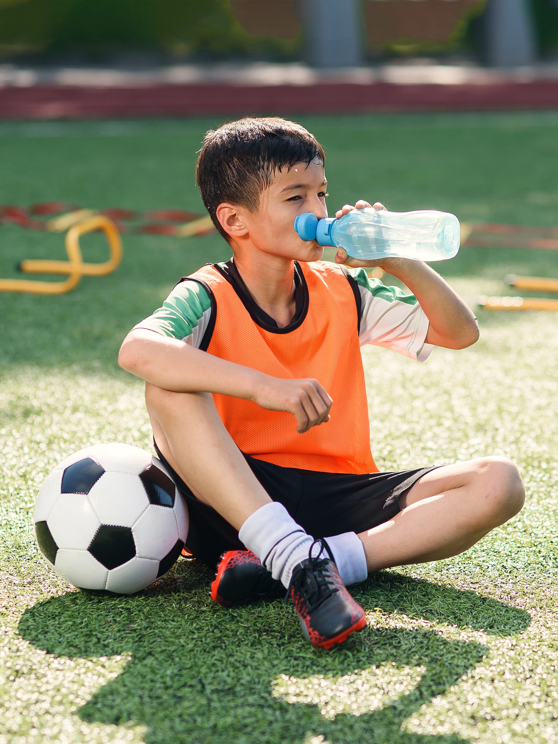 Tired teen boy in soccer uniform drinks water from plastic bottle