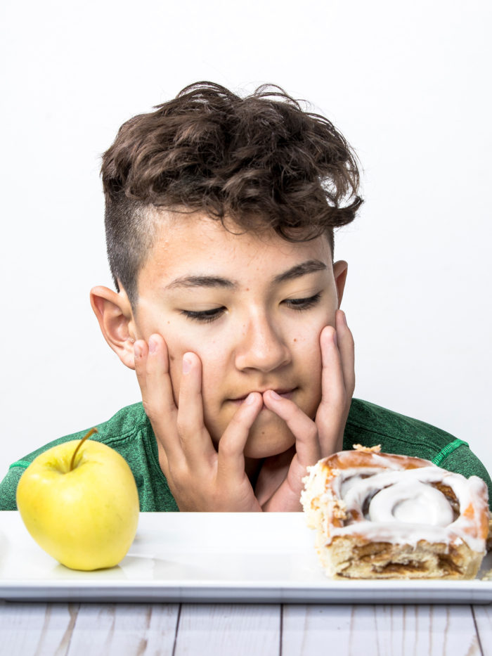 teen boy trying to decide between a healthy apple and a cinnamon roll