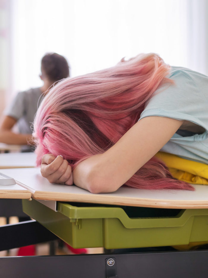 Tired teenage student asleep on her desk in school