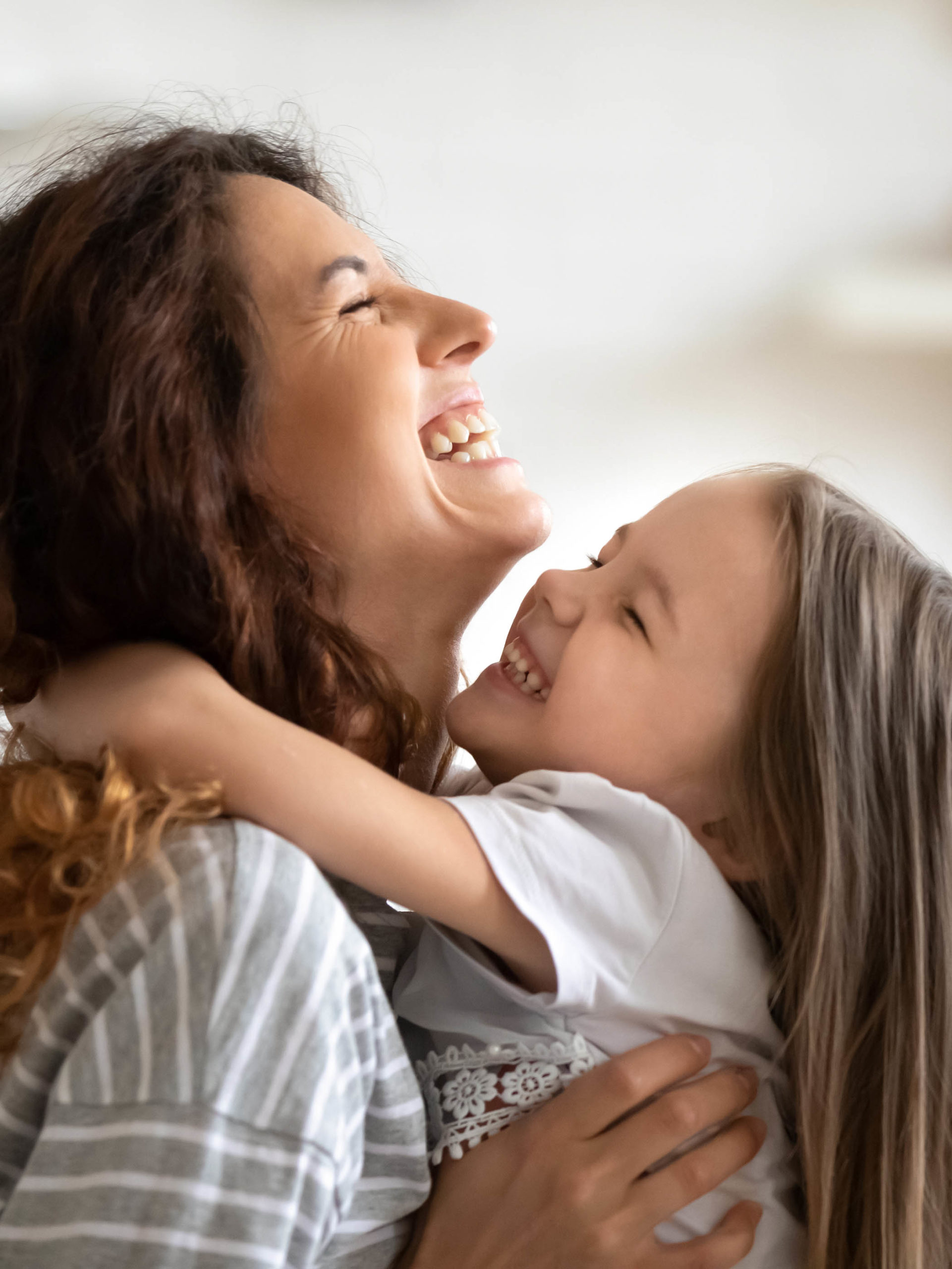 overjoyed smiling young mother and daughter hugging and laughing