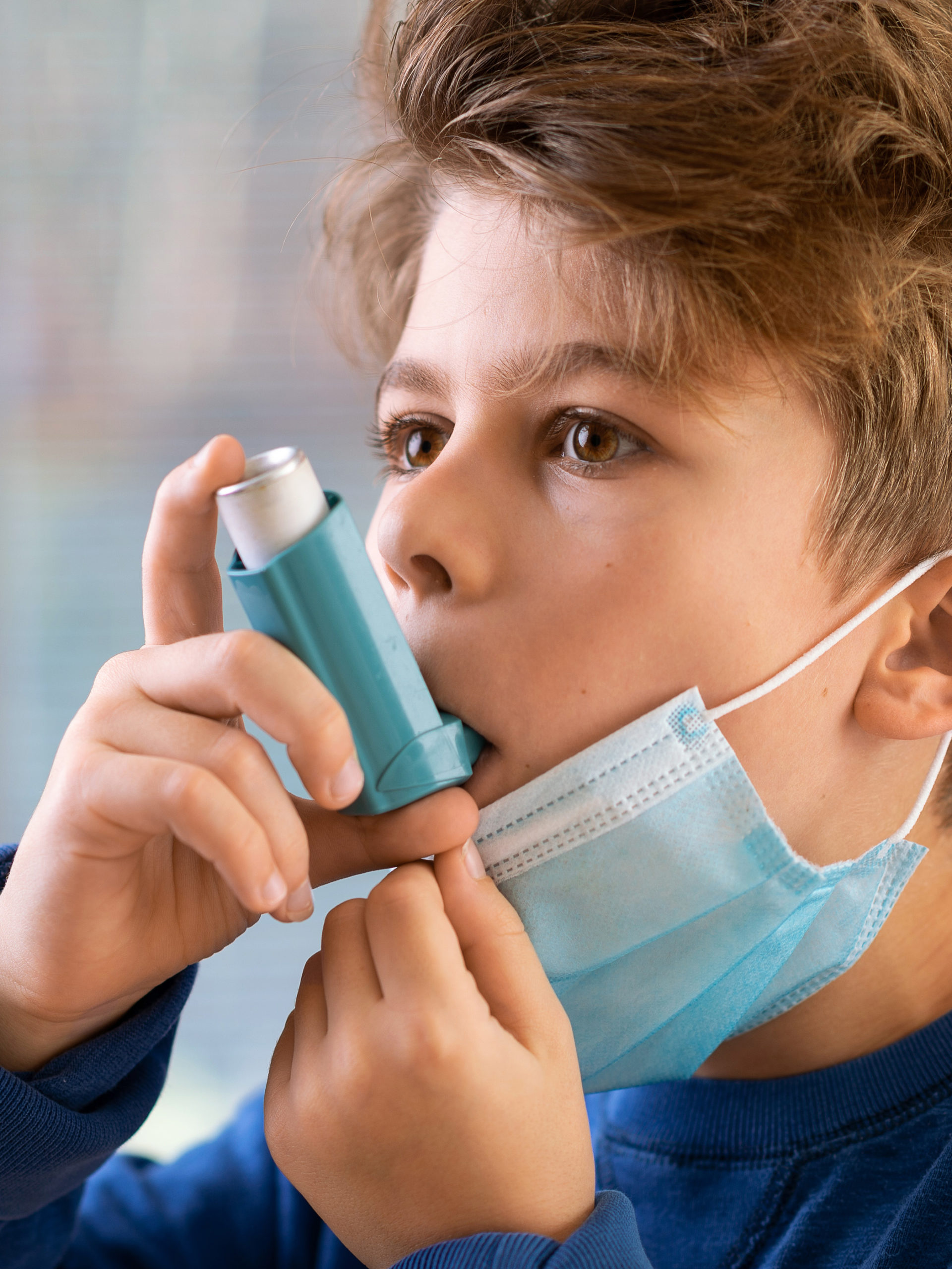 Young Boy with face mask using asthma inhaler amid Covid-19 pandemic