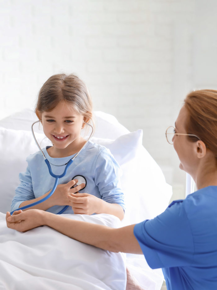 Female doctor with little girl in hospital room letting her listen to her own heart