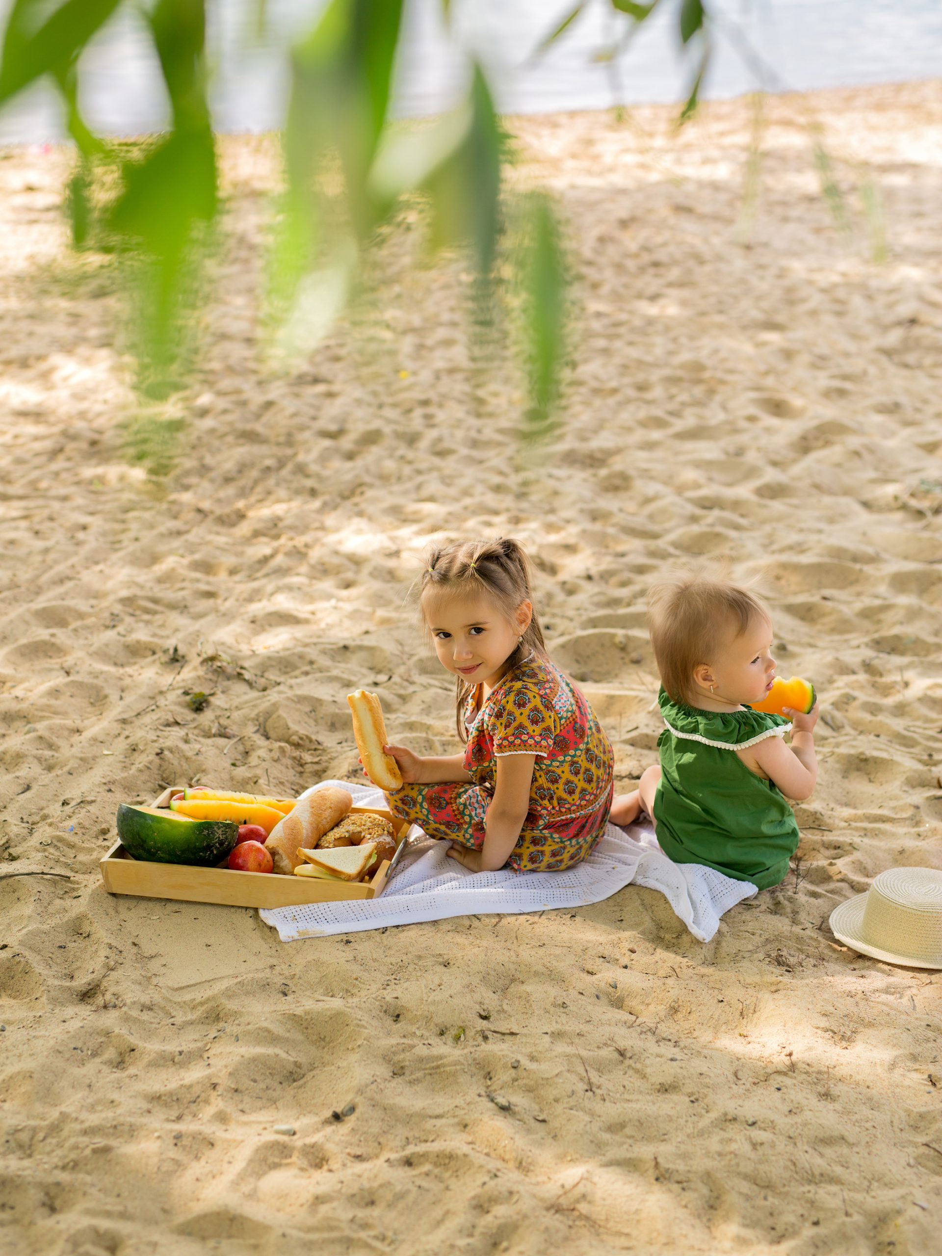 Two sisters on the beach have a picnic with fruit and sandwiches