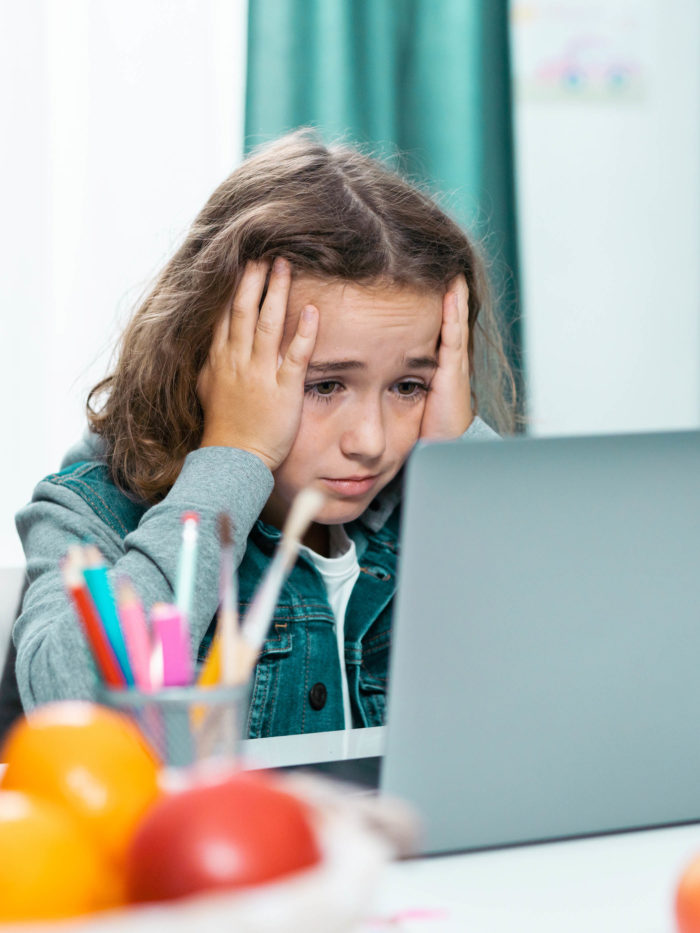 distressed young girl with hands on her face looking at her laptop