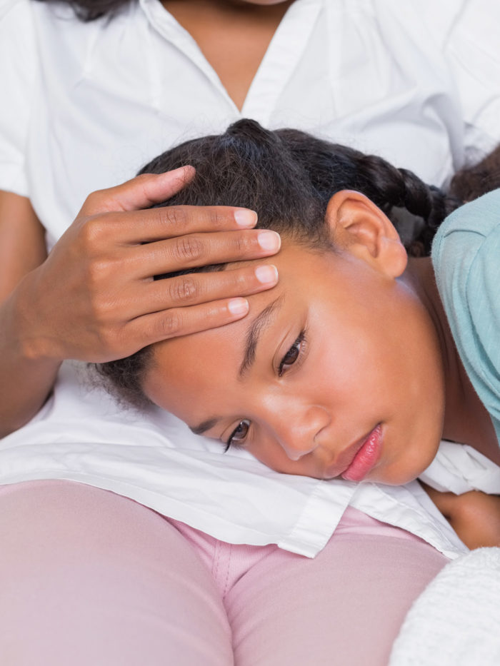 Sick daughter lying on mothers lap at home in living room