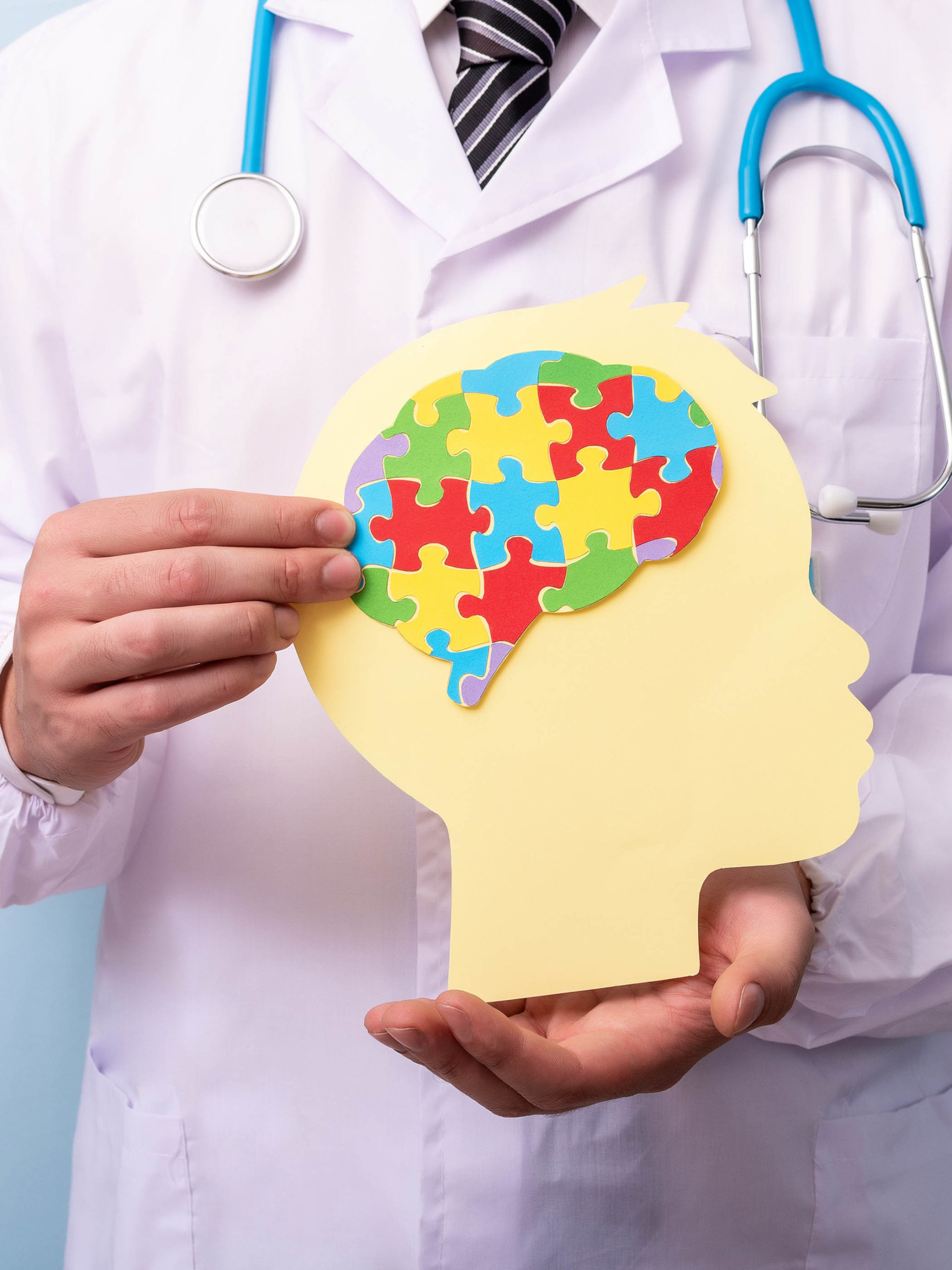 Doctor hands holding head with jigsaw puzzle brain shape to represent autism