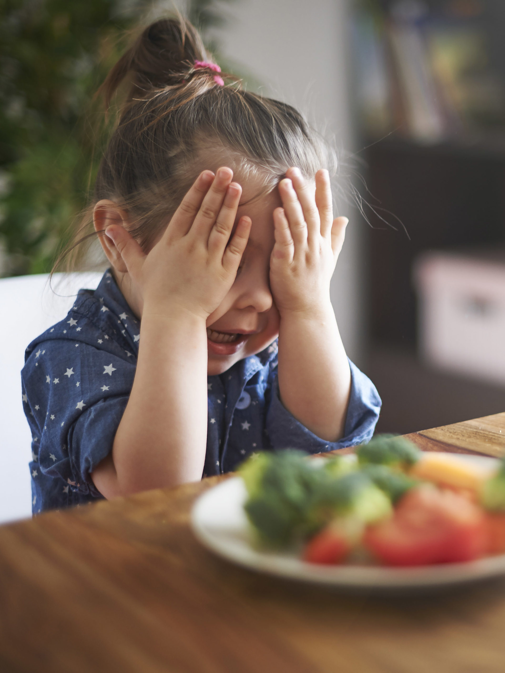 Little girl putting her hands over her eyes because she doesn't want to eat vegetables