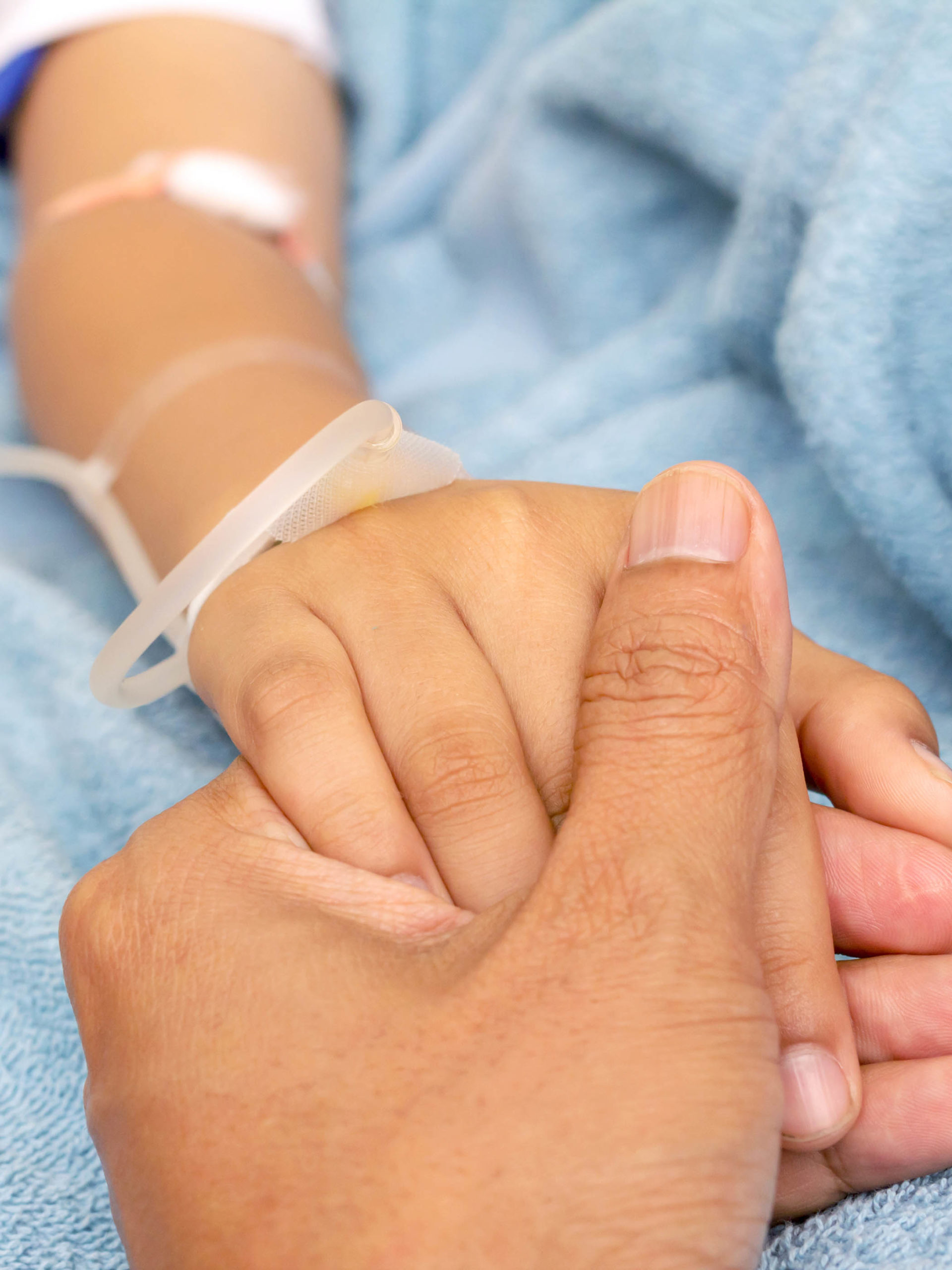 parent holding child's hand in hospital bed with IV solution in a child's patients hand