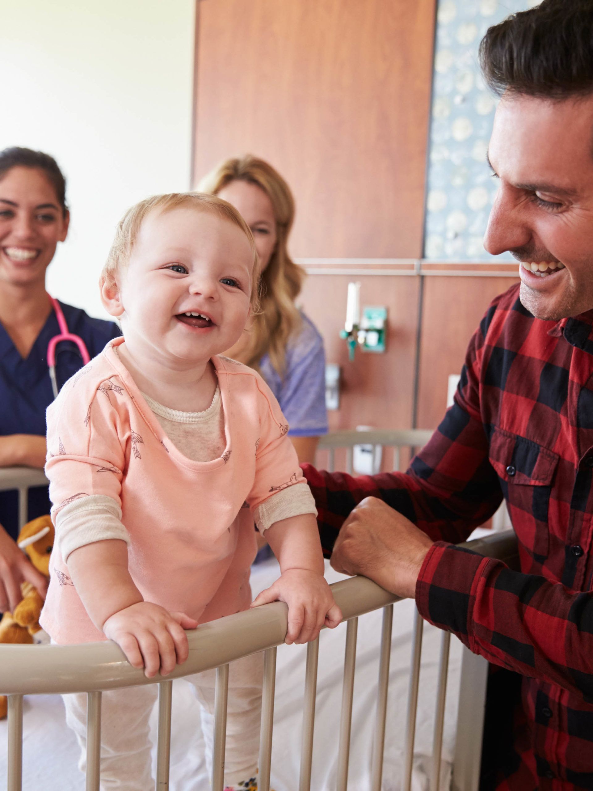 Happy toddler in hospital crib with dad, pediatrician and nurse