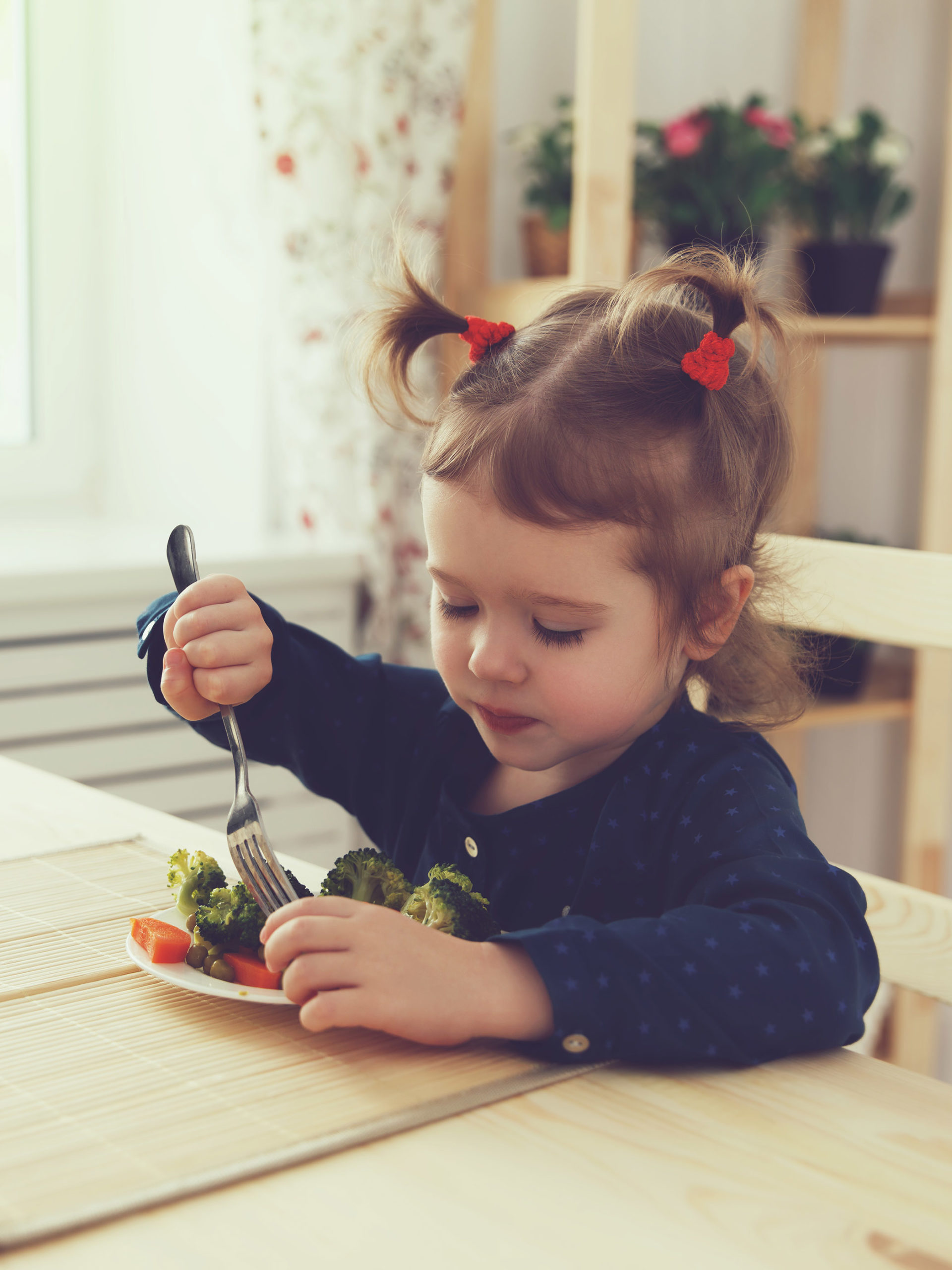 little girl eating broccoli and carrots with a fork