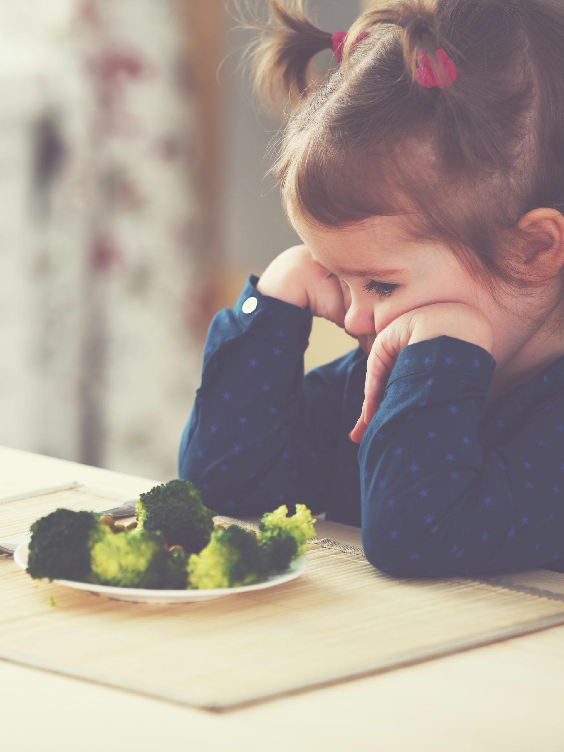 little girl refusing to eat a plate of broccoli