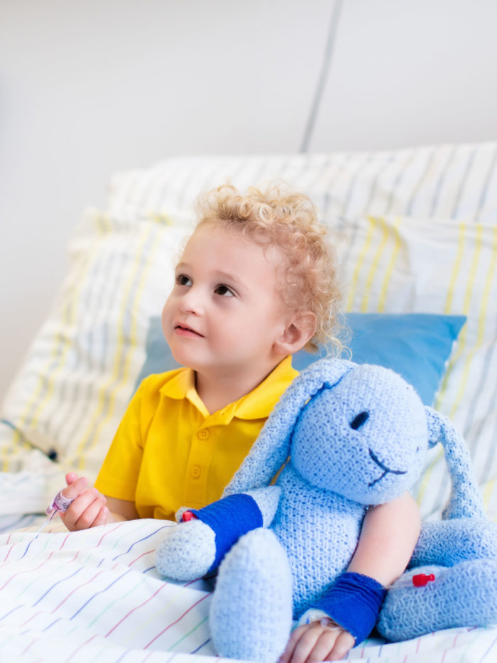 Little boy with his blue stuffed rabbit in bed in hospital room