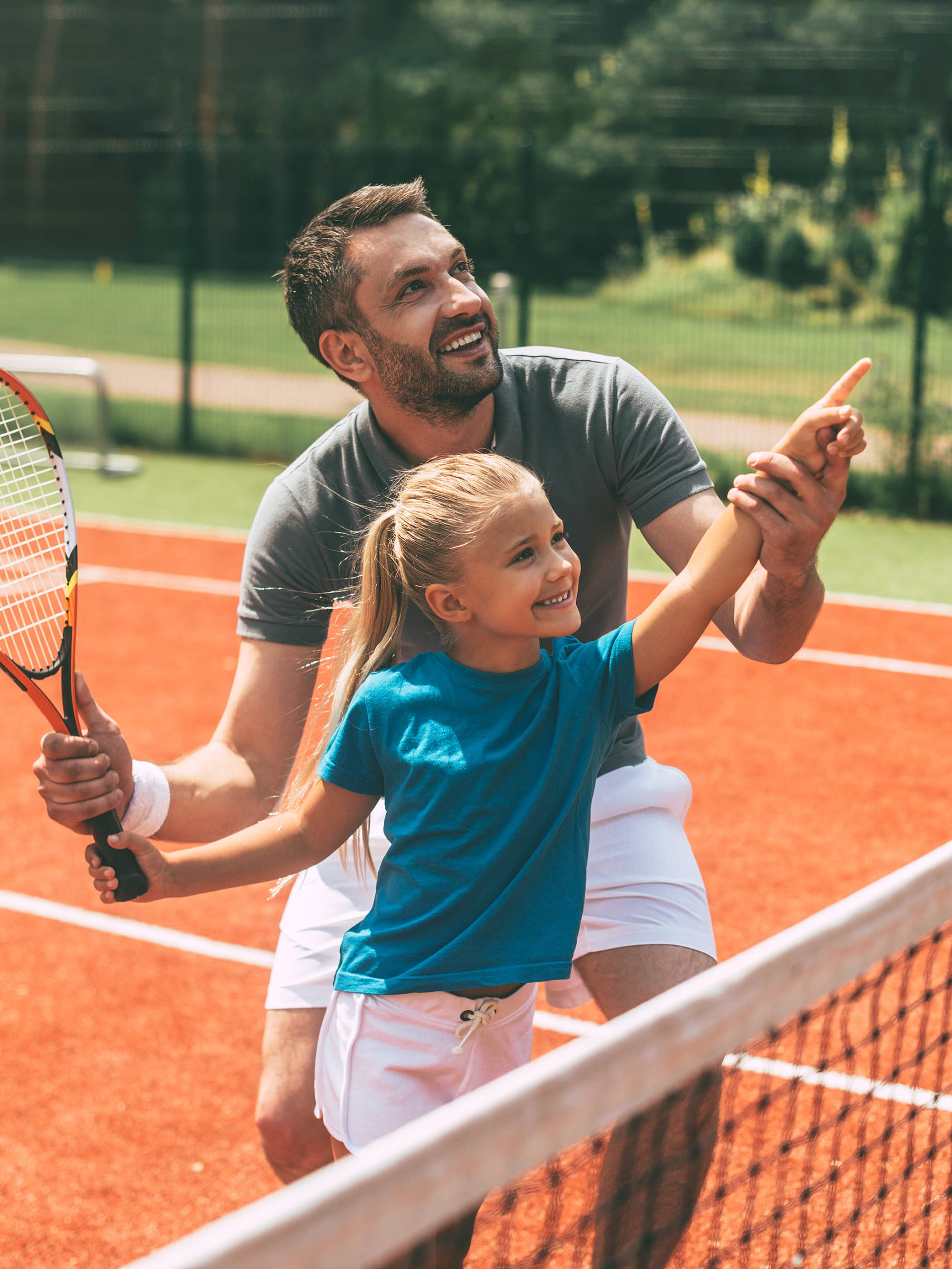 cheerful dad and daughter on tennis court, dad showing daughter how to play