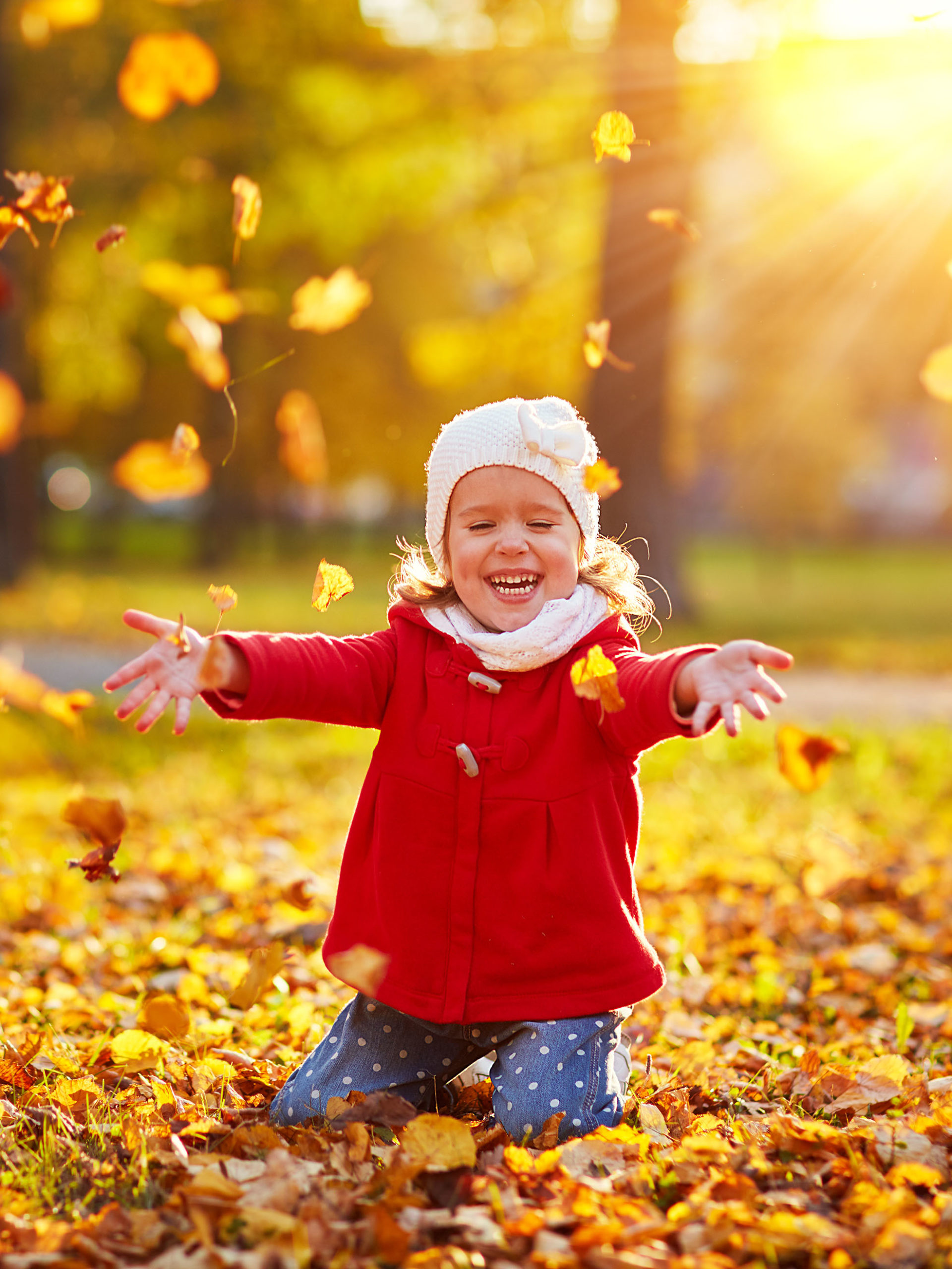 happy girl laughing and playing with leaves in autumn