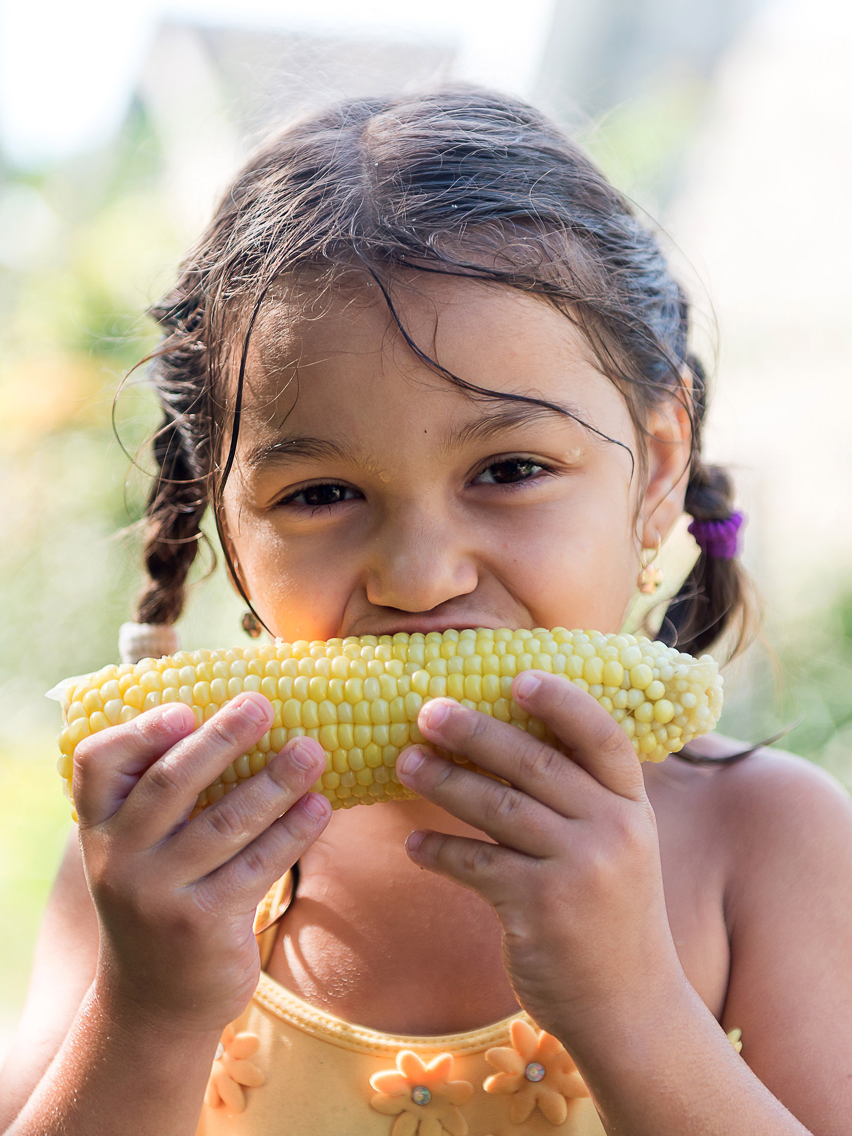 young girl eating corn on the cob on a summer day