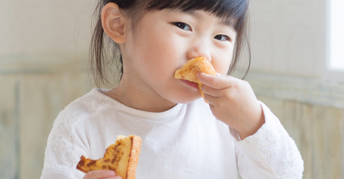 Little girl eating toast for breakfast with tea cup