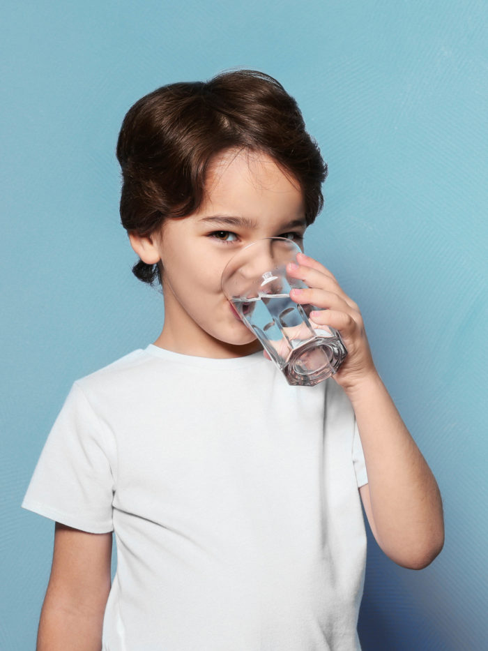 little boy smiling and drinking water from glass