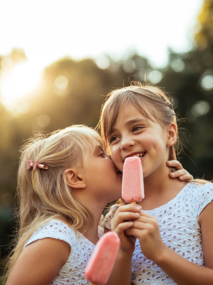 Shot of a two young girls whispering while eating ice cream outdoors