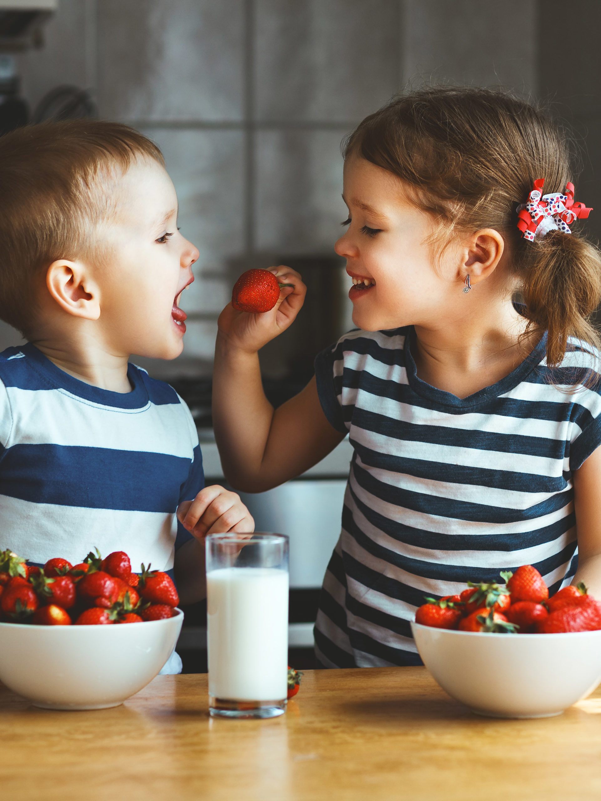 Happy children girl and boy eating strawberries with milk