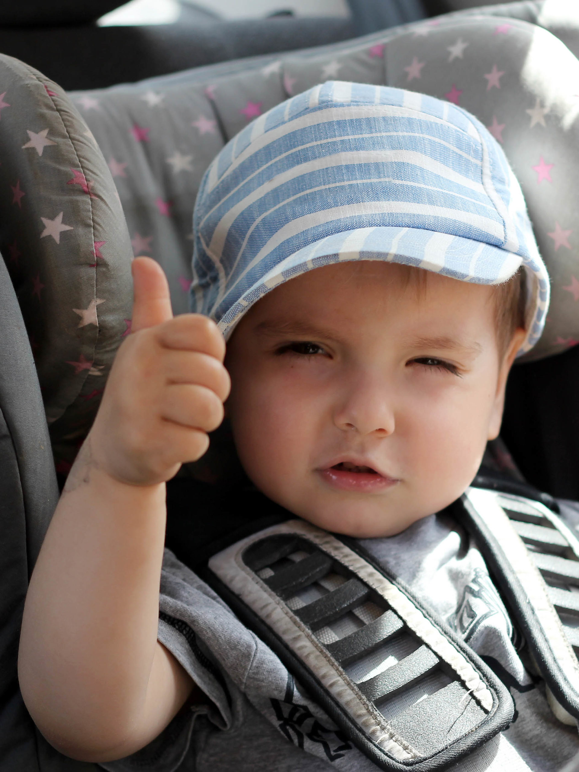 toddler boy sitting in car seat giving a thumbs up