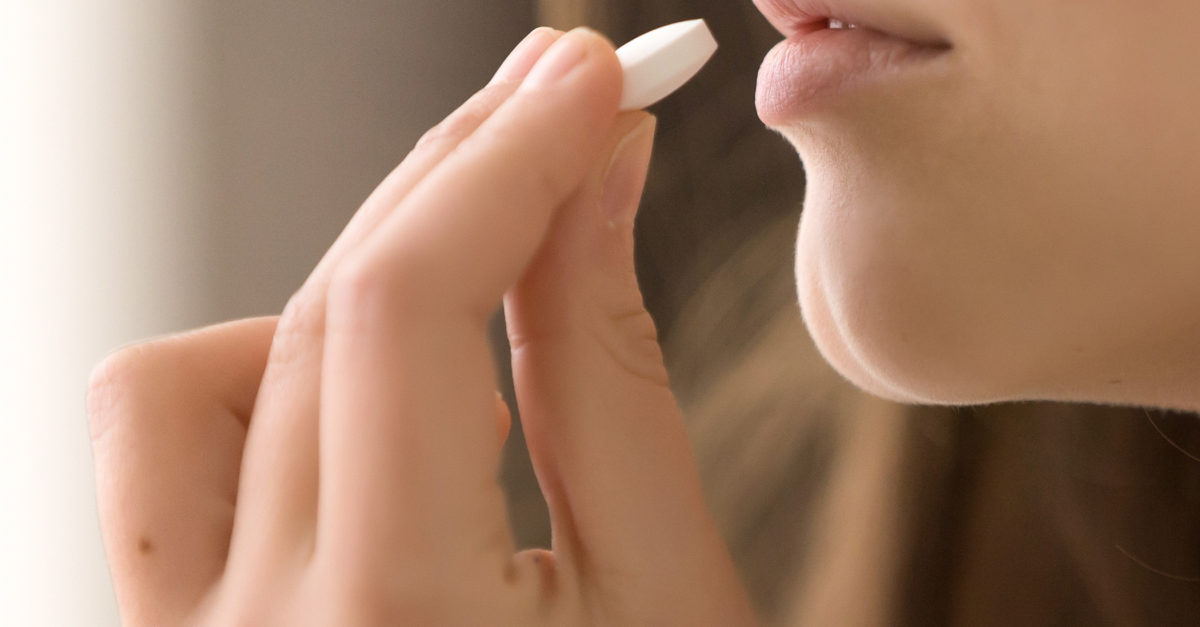 close up of woman putting white round pill in mouth