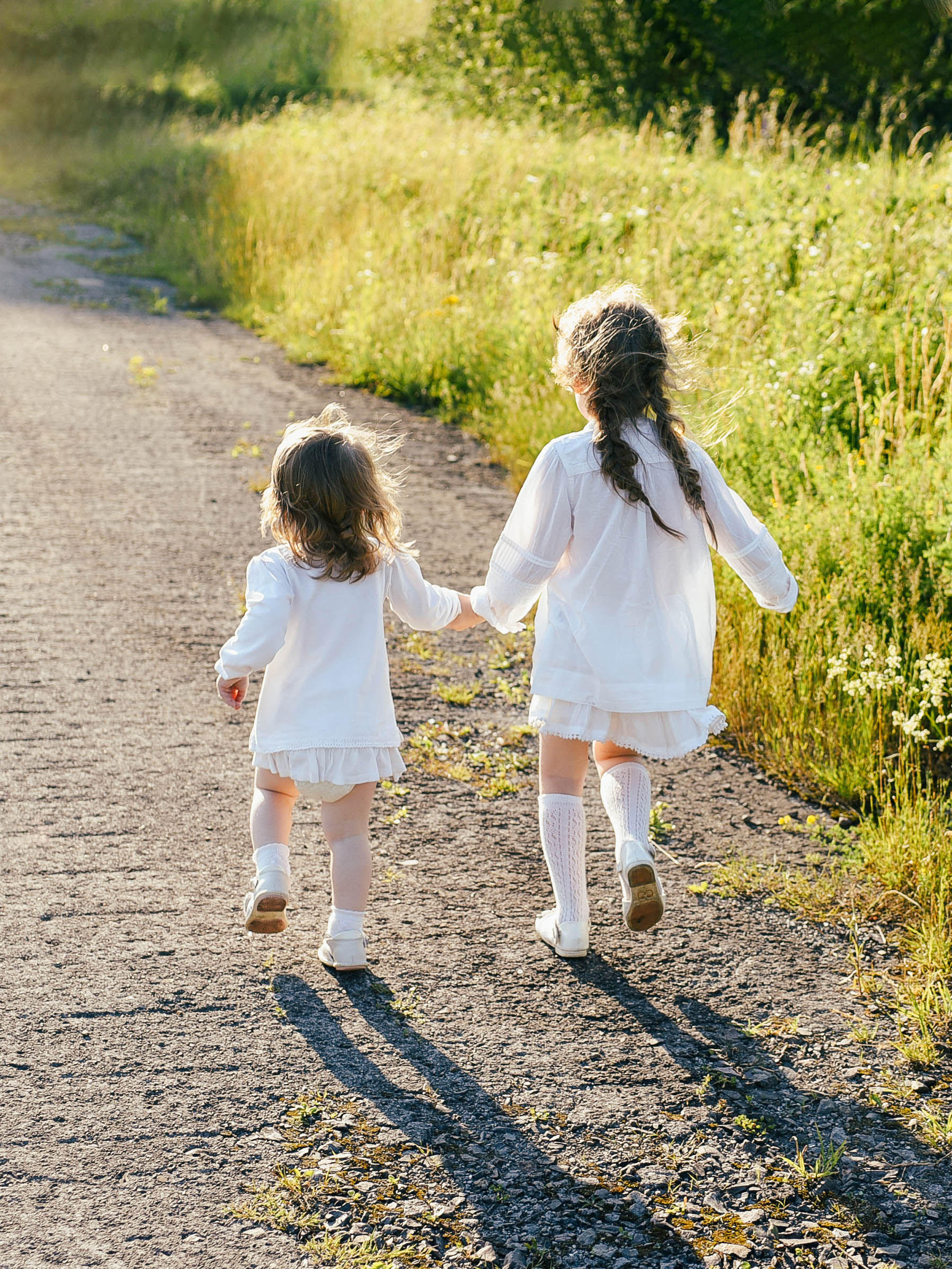 Two little sisters holding each other hands and running forward by the forest road at sunset