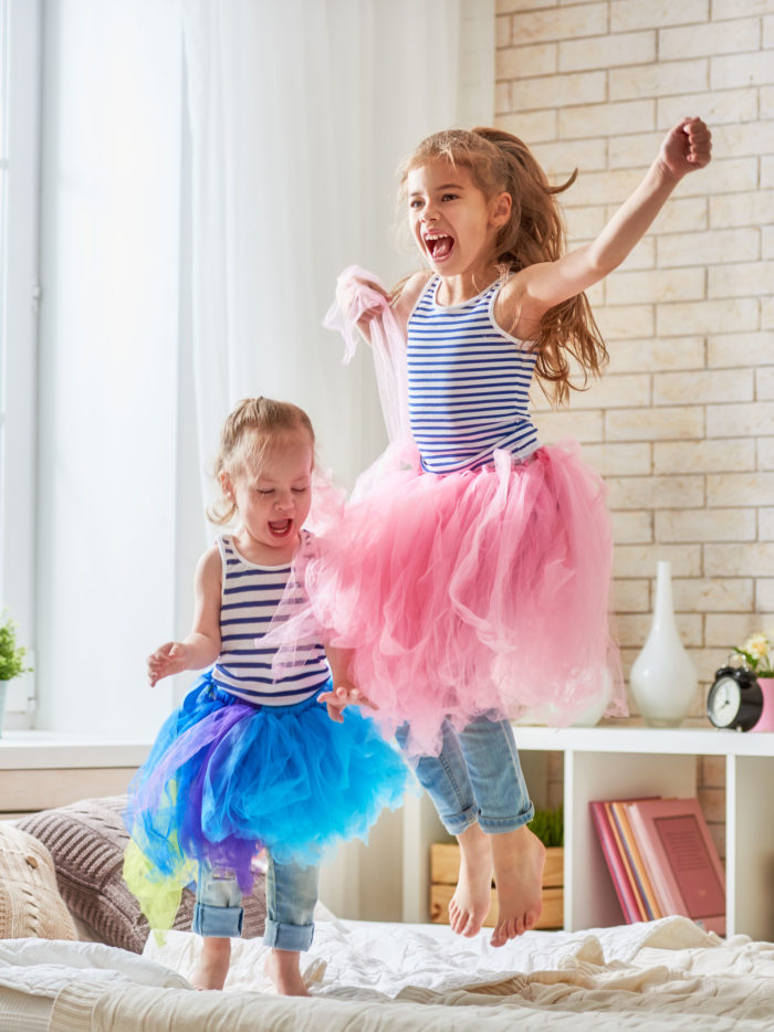 two sisters wearing tutus jumping up and down on the bed having fun