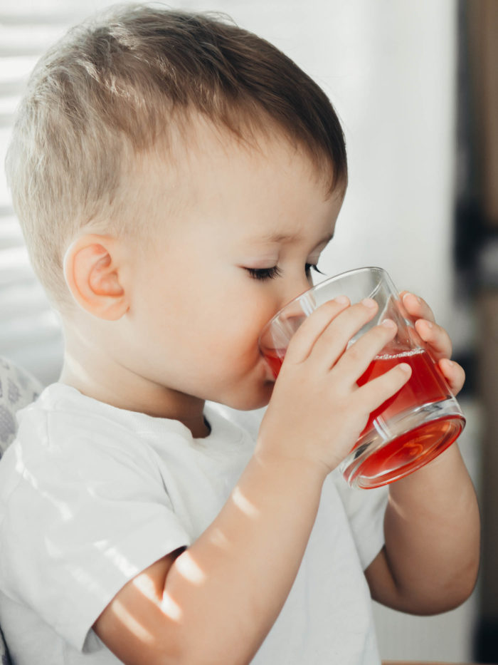 Two year boy drinking red juice from a glass
