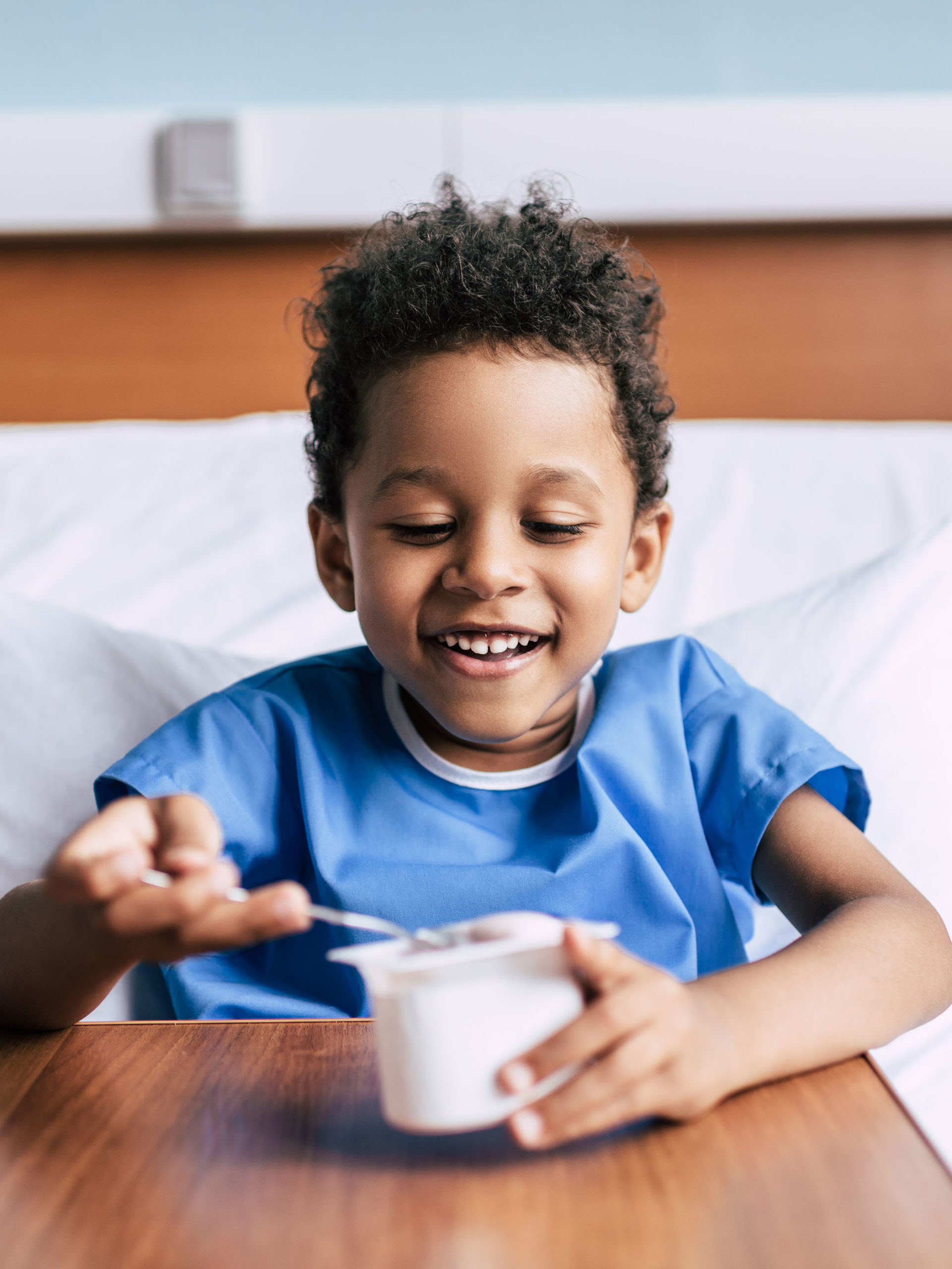 boy eating yogurt while resting in hospital bed