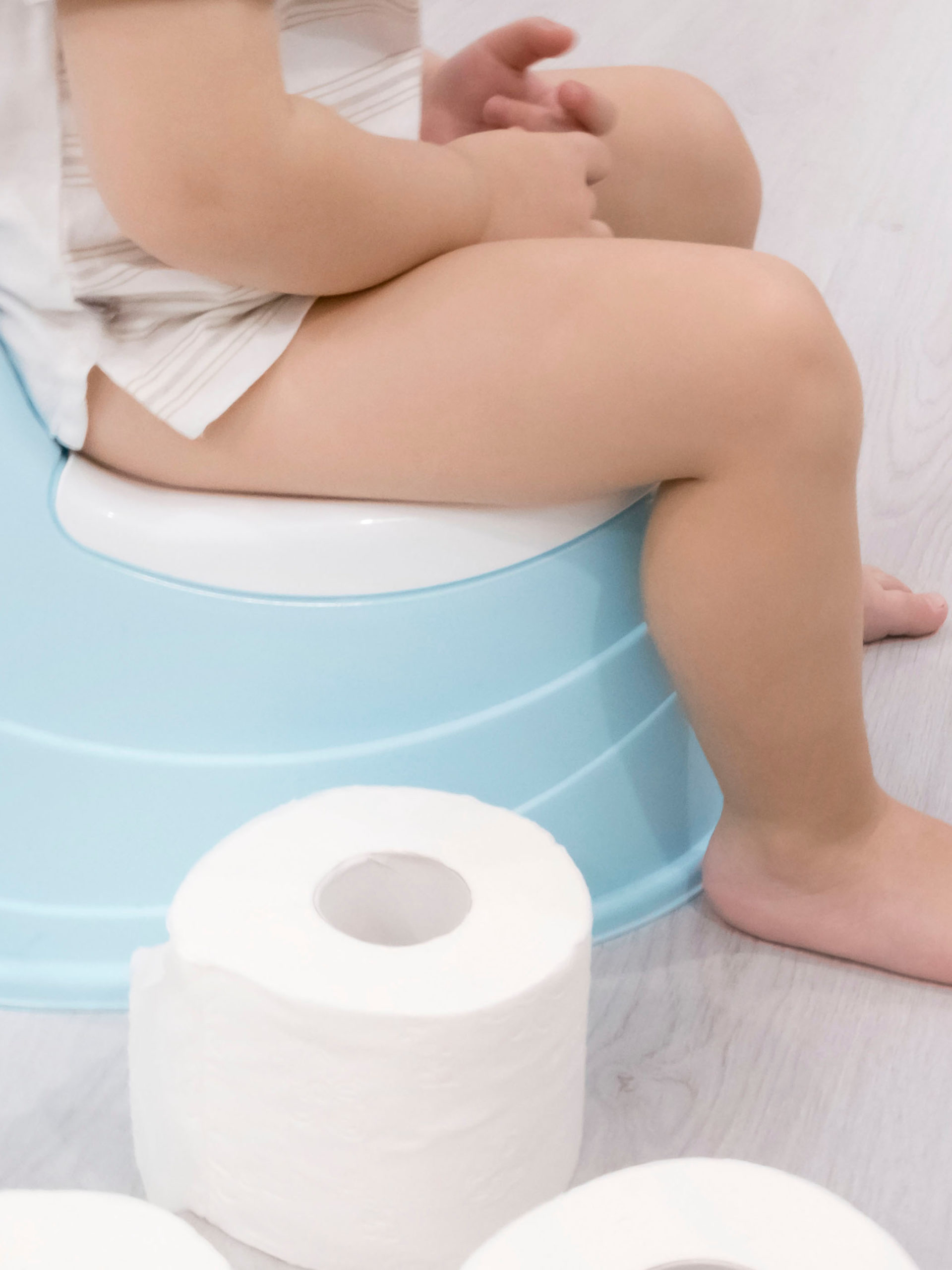 smiling baby sitting on potty with toilet paper rolls