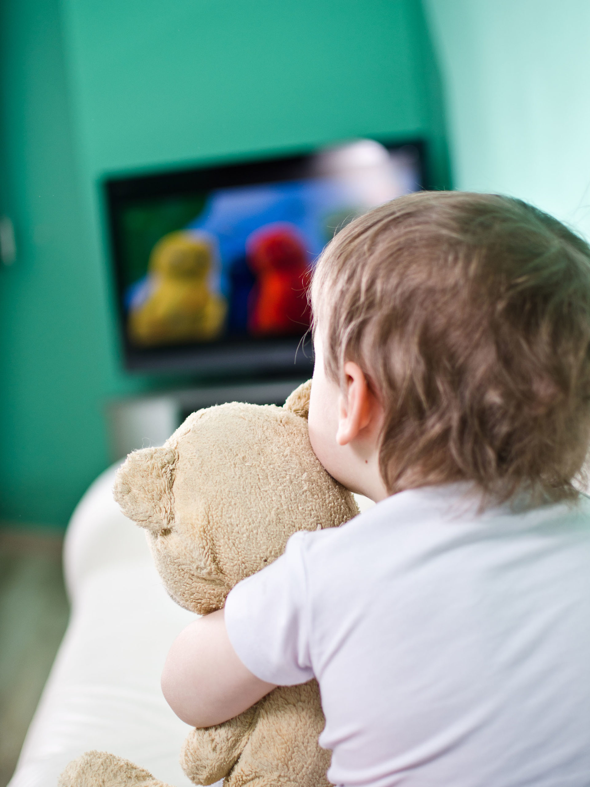 young boy and his teddy bear watching TV
