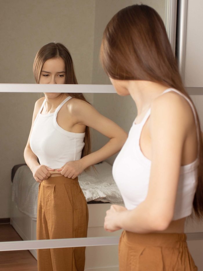 girl measures waist while looking in the mirror
