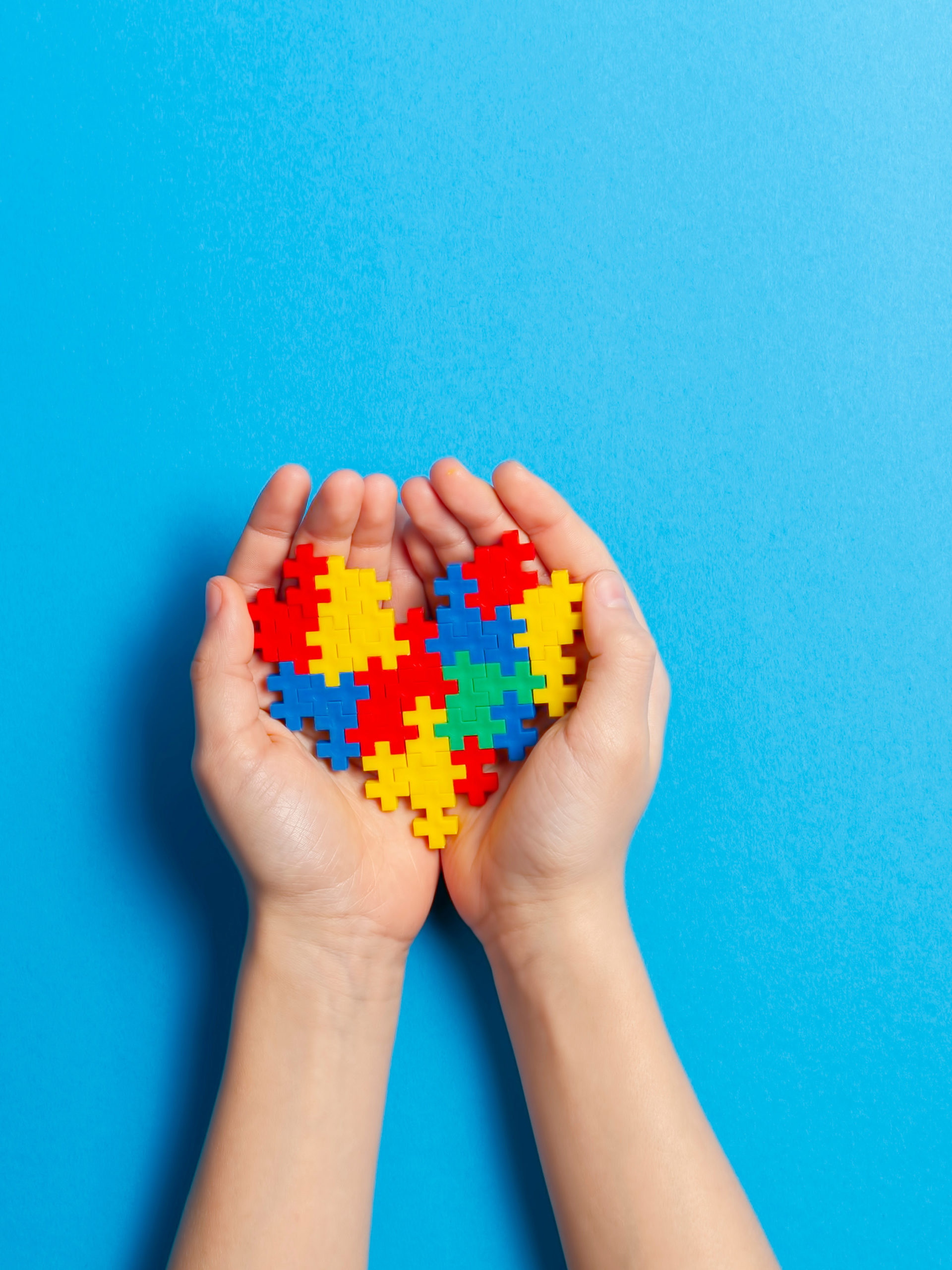 hands holding colored puzzle pieces representing autism