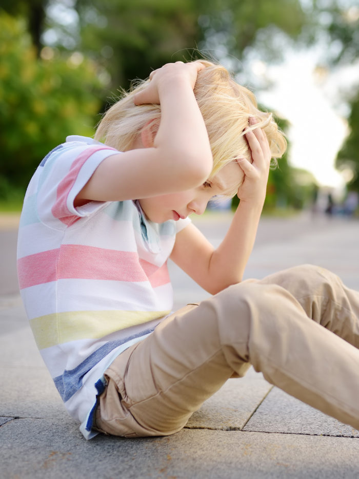 boy holds head while sitting on the ground