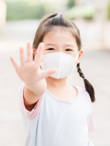 Little girl wearing mask holds out hand in front of her