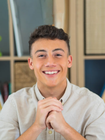 Male teen smiles at the camera in front of bookcase
