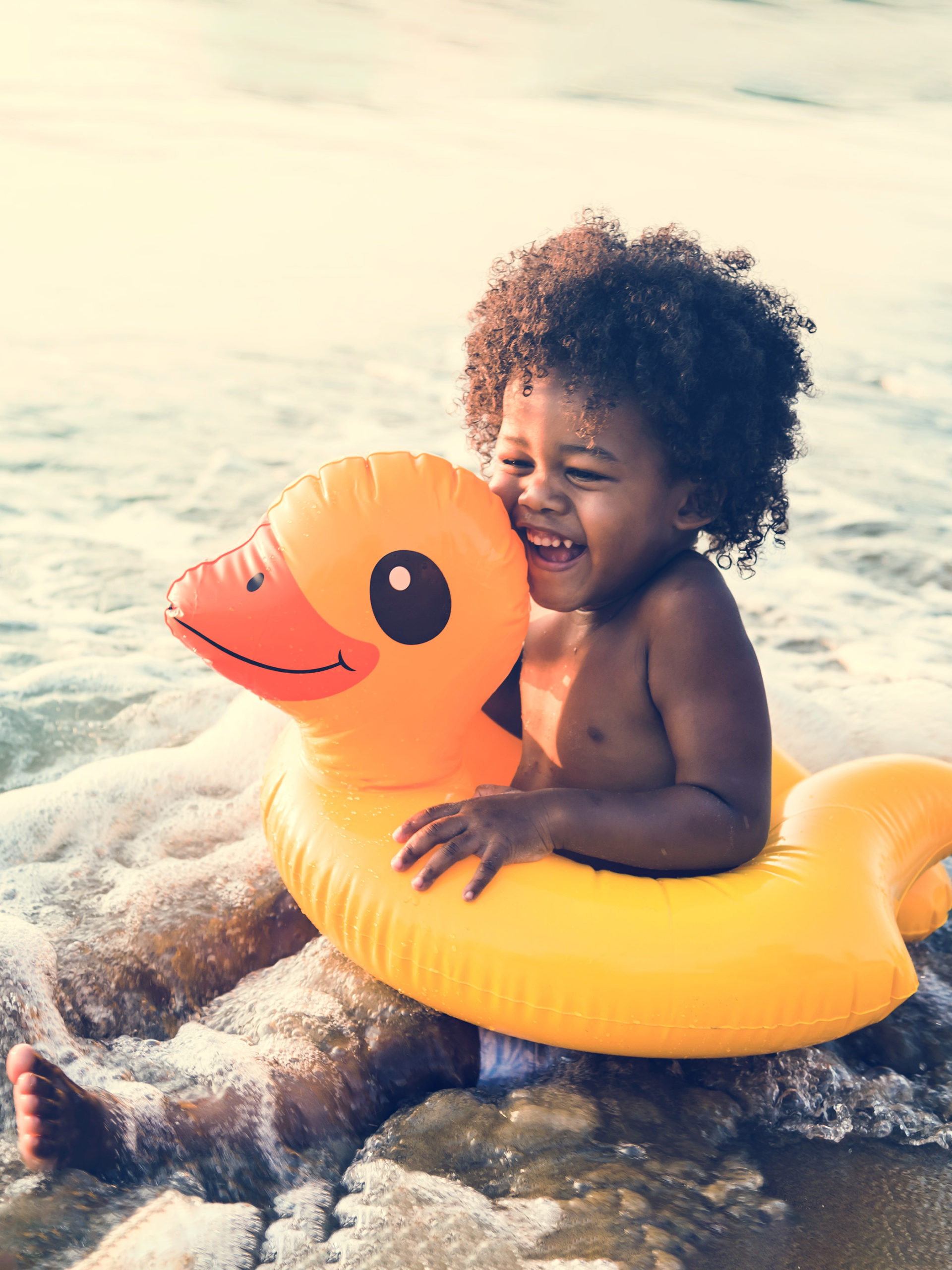 Little boy smiling in ocean water in a yellow duck floaty