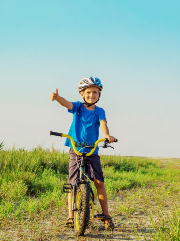 kid in field on a bike with a thumbs up