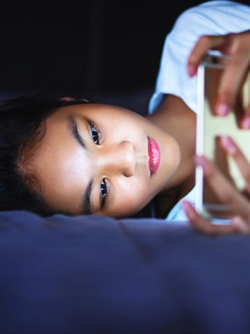 girl laying down in bed at night - looking at bright light on phone