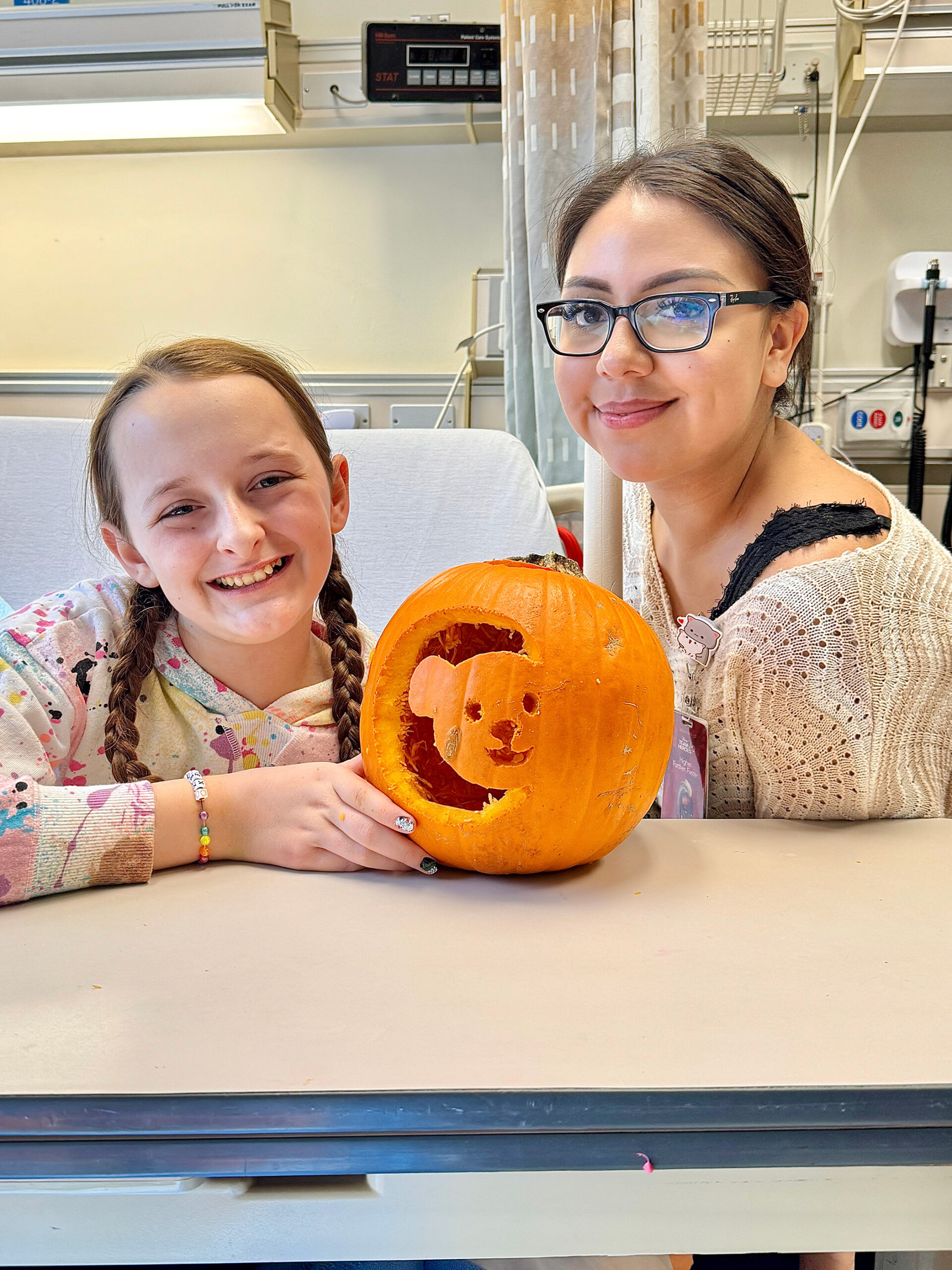 CHOC patient Alex and child life specialist Karla smile with a pumpkin that is carved with Choco bear on it