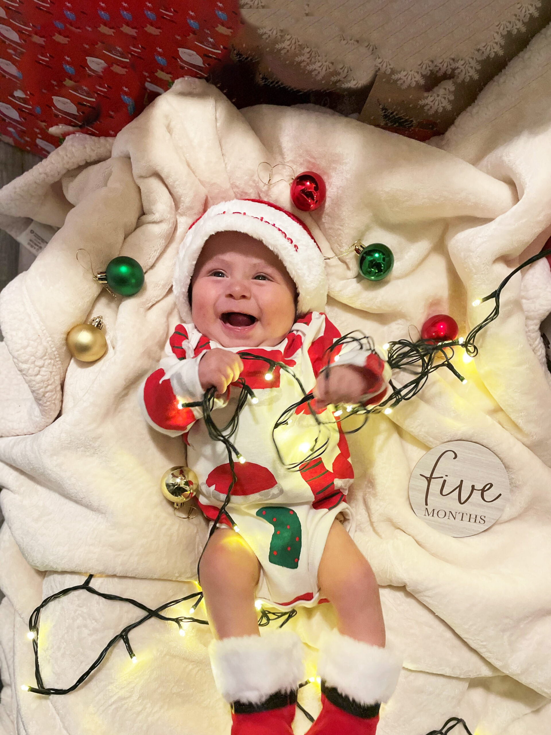 Damian smiling with lights and ornaments, celebrating 5 months of age