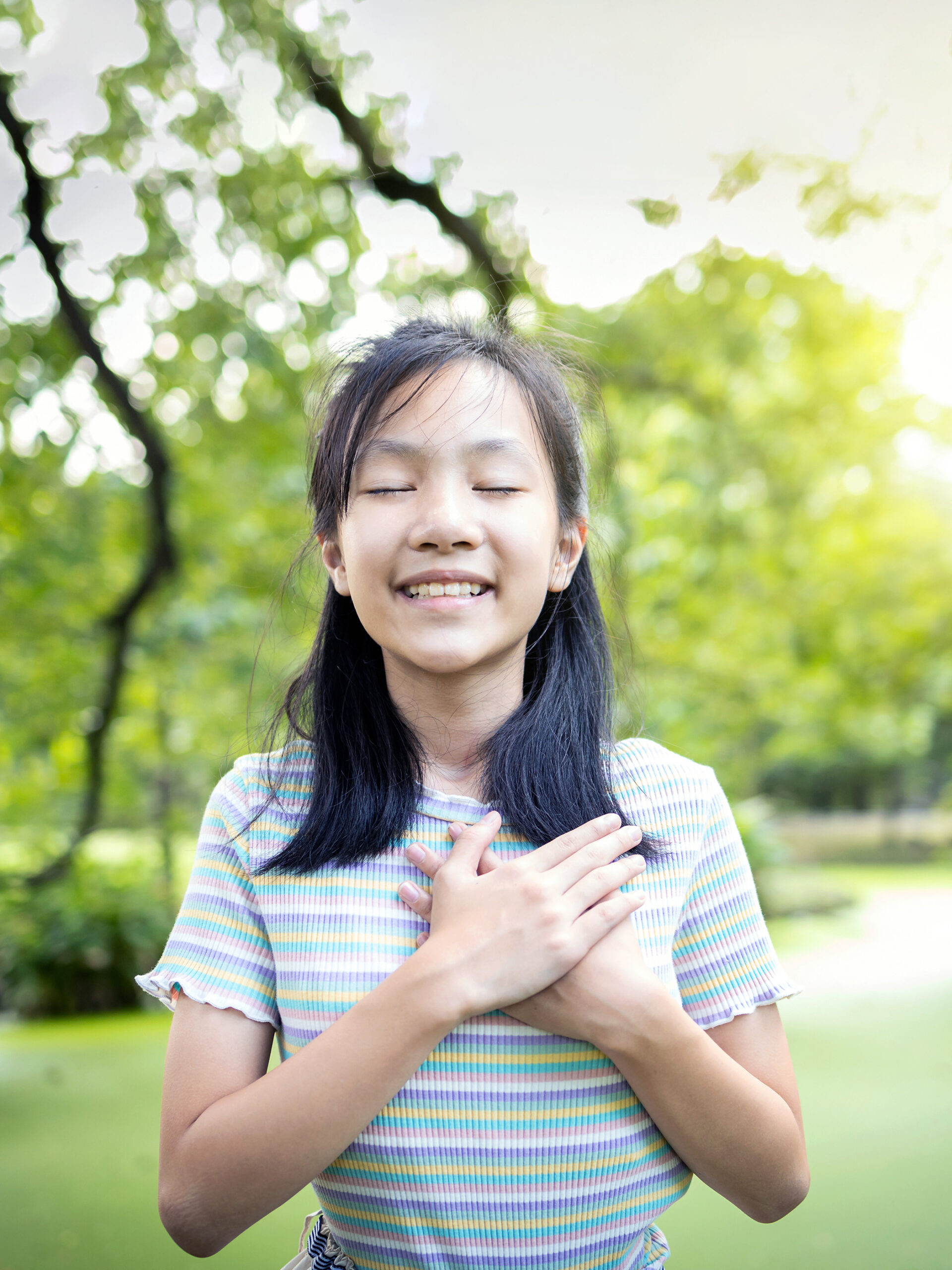 Child closes eyes with hands over heart, looking content - practicing mindfulness with kids