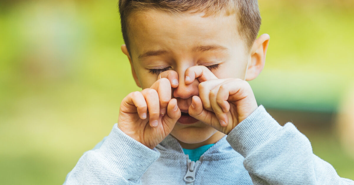 Child rubbing nose while standing outside - How to manage seasonal allergies in kids