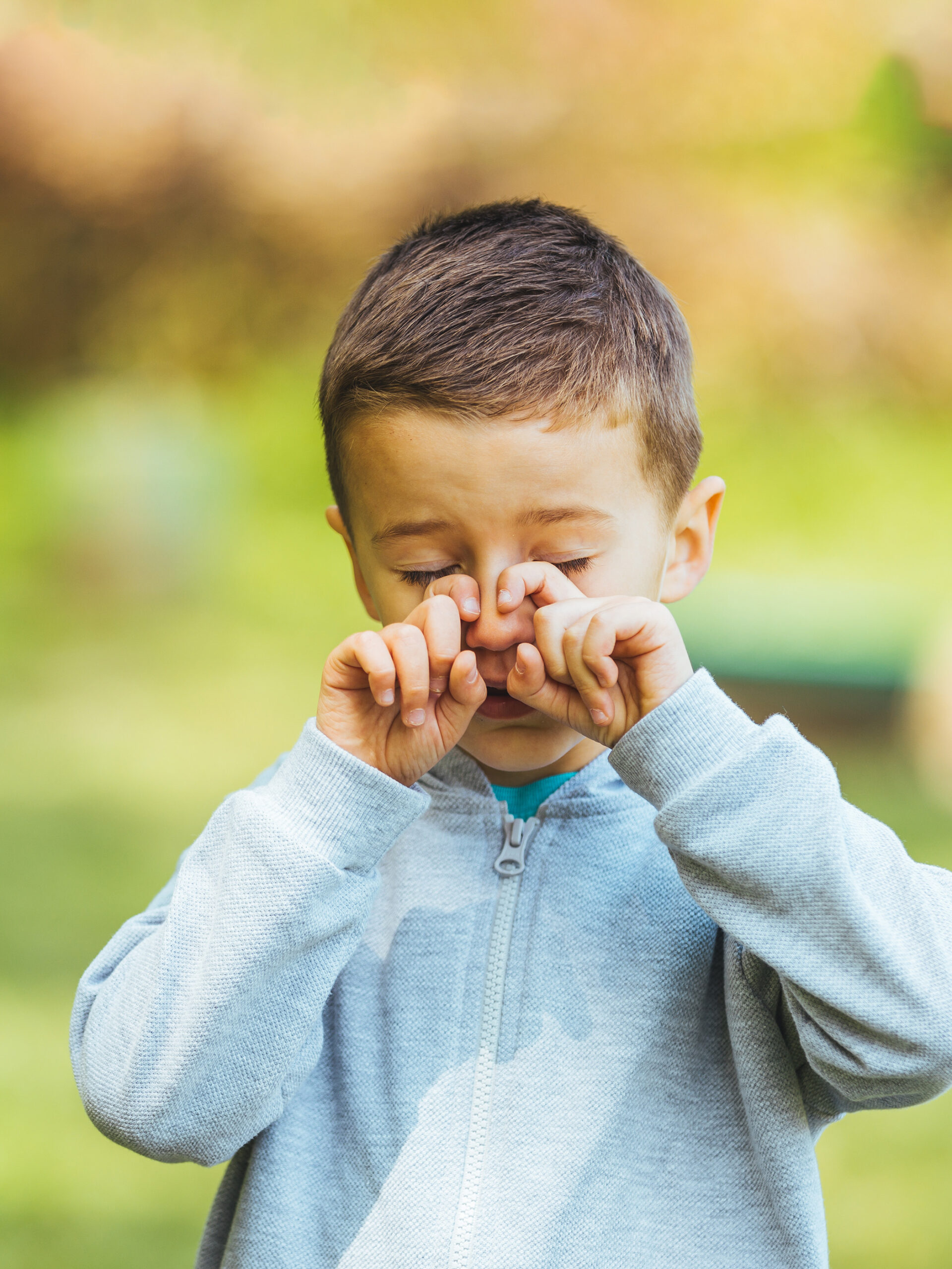 Child rubbing nose while standing outside - How to manage seasonal allergies in kids